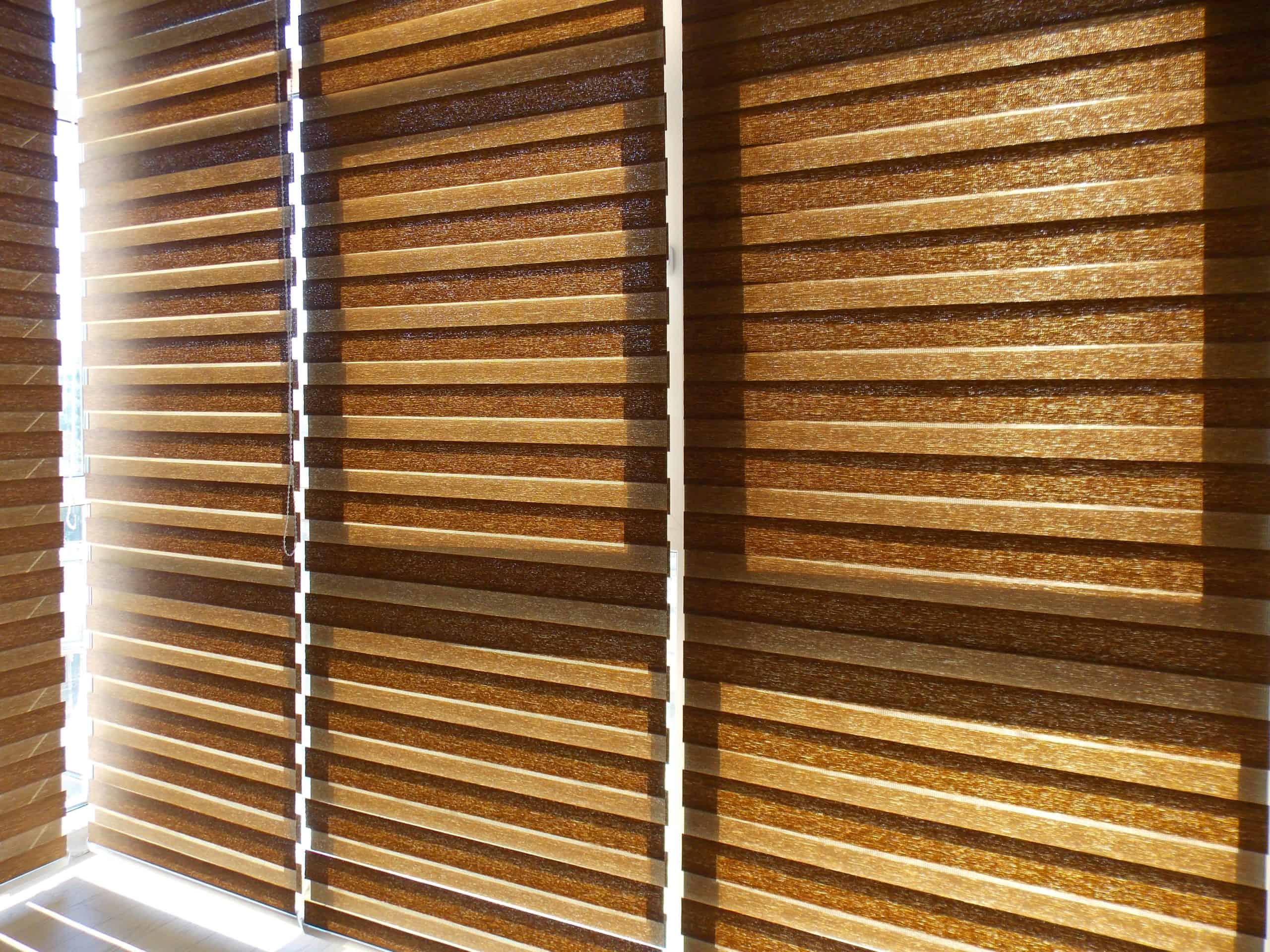 Sunlight filters through partially closed, horizontal wooden blinds, casting striped shadows on the window sill. The warm, golden tones create a cozy, inviting atmosphere.