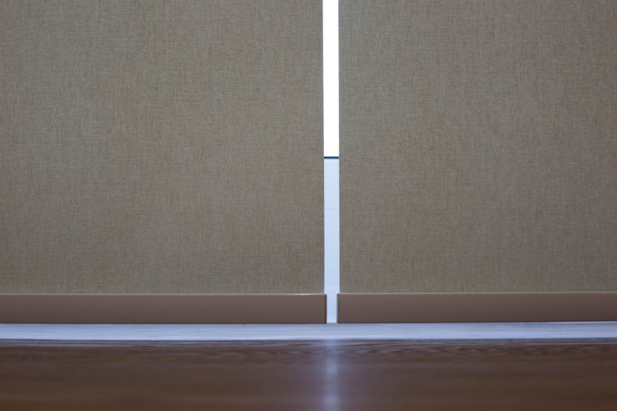 A close-up view of two beige sliding doors slightly parted, revealing a narrow strip of light between them, with a wooden floor visible at the bottom.