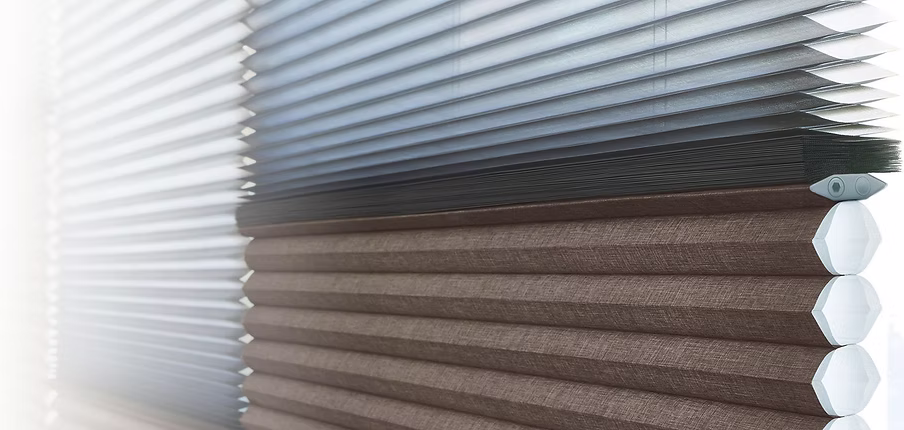 Close-up of a window with dual-layered pleated blinds; the top section is made of light gray translucent material, while the bottom section is a darker, opaque brown fabric.