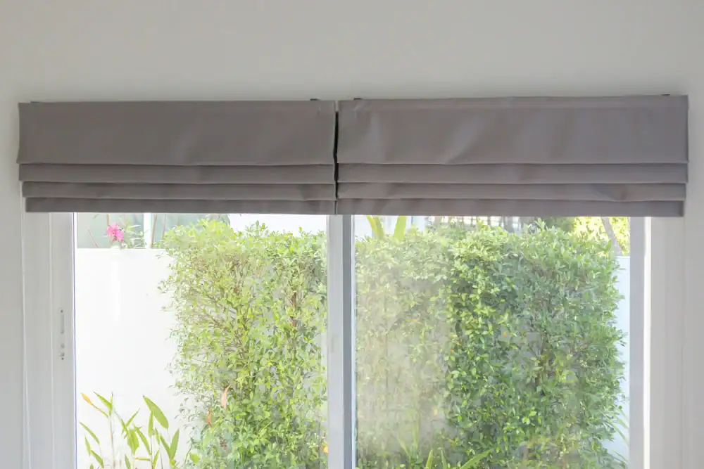 Bright gray window shades installed on a large window with lush greenery outside.